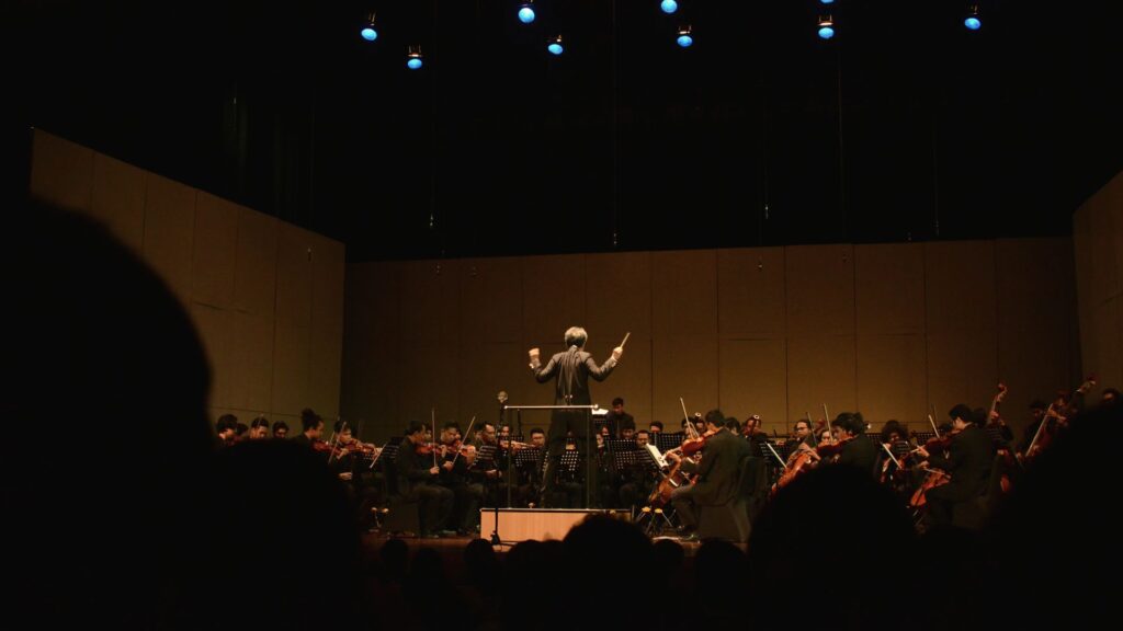 Director dirigiendo una orquesta en un auditorio