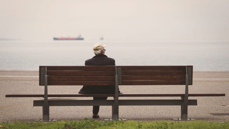 Hombre mayor sentado en un banco mirando al mar