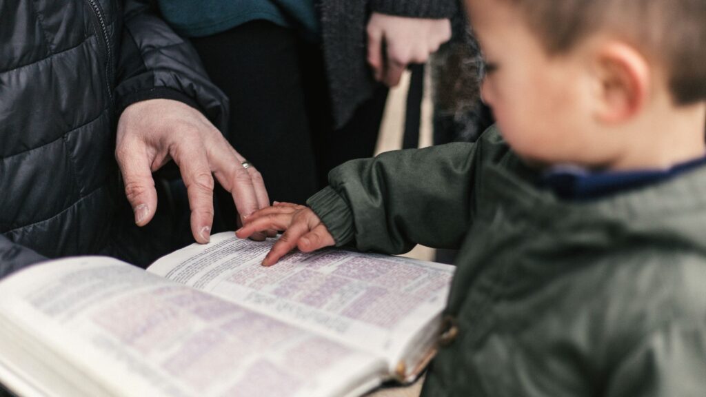 Niño señalando un libro abierto junto a la mano de un adulto